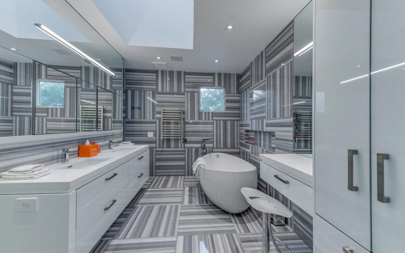 White bathroom countertop with large mirror, white vanity, bathtub, small mirror, and chair
