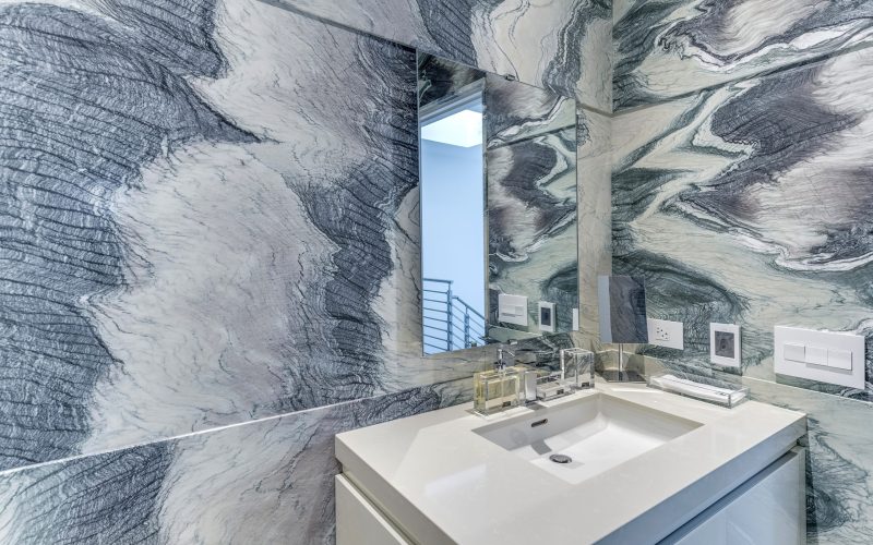 White bathroom sink countertop with mirror, stone wall, and switch board in Glenview Princeton Club remodel