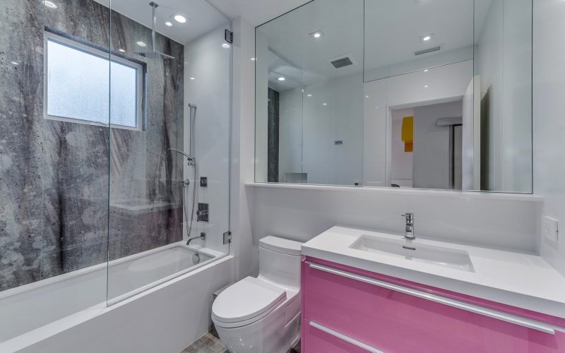 White bathroom sink with pink vanity, mirror, toilet, and bathtub with shower and grey wall stone in Glenview Princeton Club remodel