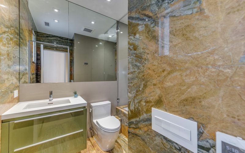 White bathroom sink with green vanity, mirror, toilet, and bathtub with yellow wall stone and hand shower in Glenview Princeton Club remodel