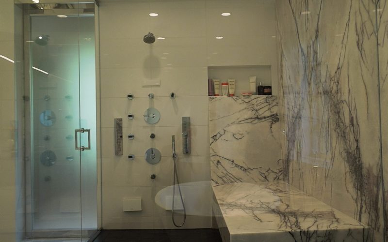 Black bathroom floor with white wall tiles, shower, and waterfall stone bench